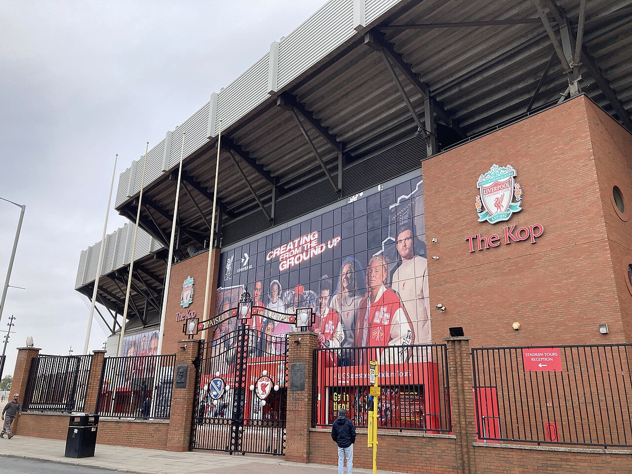 The Kop stand at Anfield from the street, with the Liverpool FC crest, the Paisley Gateway and the stadium tours entrance